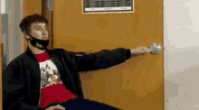 a man wearing a mask is sitting in front of a door holding a doorknob .