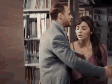 a man and a woman are hugging in front of a bookshelf in a library .