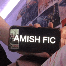 a person holding a cell phone that says amish fic on it