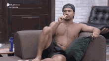 a shirtless man sits on a couch with playplus written on the bottom right