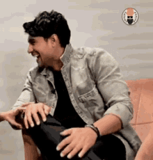 a man is sitting on a couch holding another man 's hand and laughing .