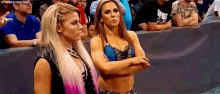 two women are standing next to each other in a wrestling ring with their arms crossed in front of a crowd .