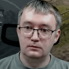 a man wearing glasses and a gray shirt is sitting in a chair .