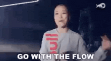 a woman is dancing in a dark room with the words `` go with the flow '' written on the screen .
