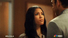 a man and a woman are looking at each other with a nbc logo behind them