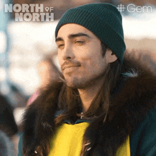 a man with long hair is wearing a green beanie and a yellow jacket with a fur collar