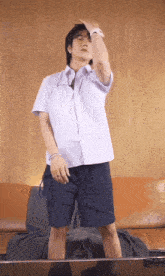 a man in a white shirt and blue shorts is standing in front of a brown couch