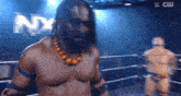 a man with long hair is standing in a wrestling ring with the word nx on the wall behind him .