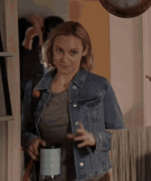 a woman wearing a denim jacket is holding a coffee mug