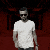 a man wearing sunglasses and a white t-shirt stands in front of a red background