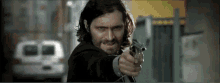 a man with long hair and a beard pointing a gun