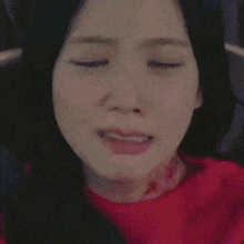 a close up of a woman 's face with her eyes closed and a red sweater on .