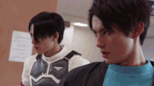 two young men are standing next to each other in a room and one is wearing a blue shirt