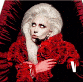 lady gaga is wearing a red coat with red roses on it and a microphone in her mouth .