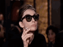 a woman wearing sunglasses is smoking a cigarette in a restaurant .