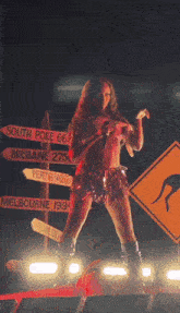 a woman stands in front of a sign that says south pole 66 brisbane 275 perth 1482 km and melbourne 194
