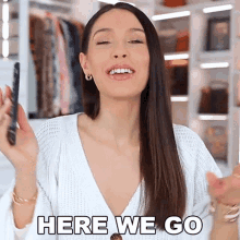 a woman is holding a cell phone and saying `` here we go '' while standing in front of a closet .