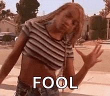 a woman in a striped crop top and shorts is standing on a sidewalk with her arms outstretched .