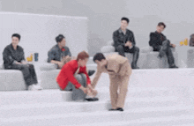 a man in a red jacket is kneeling down next to another man in a tan suit .
