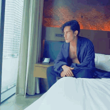 a man sitting on a bed looking out a window