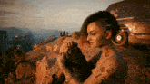 a woman with a shaved head sits on a rock in front of a california van