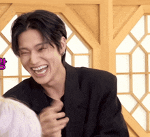 a man in a black jacket is laughing in front of a window with a pink sticker that says ' g '