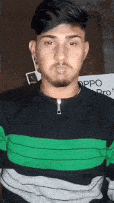 a man wearing a black and green striped shirt stands in front of a sign that says oppo pro 5