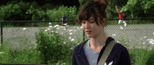 a woman is standing in front of a chain link fence with flowers in the background