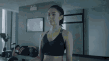 a woman in a black sports bra is standing in a gym looking at the camera .