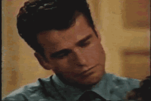 a man in a blue shirt and tie looks down