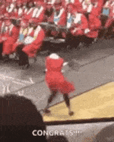 a woman in a red dress is dancing on a stage in front of a crowd at a graduation ceremony .