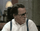 a man wearing suspenders and glasses is looking at the camera