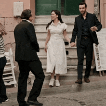 a man in a suit and a woman in a white dress are holding hands