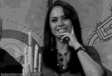a black and white photo of a woman smiling with her hand on her face .