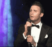 a man in a tuxedo is singing into a microphone on stage