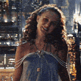 a woman in a blue dress is smiling in front of a city at night