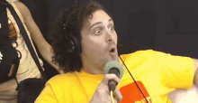 a man in a yellow shirt is talking into a microphone