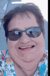 a woman wearing sunglasses and a floral shirt smiles at the camera