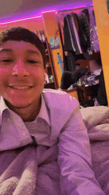 a man in a white shirt is smiling while laying on a bed under a blanket
