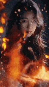 a woman is standing in front of a fire and looking at it .