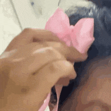 a close up of a person holding a pink bow in their hair .