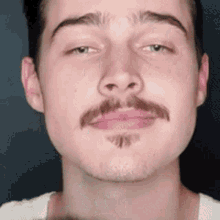 a close up of a man 's face with a mustache and a white shirt .
