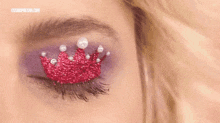 a close up of a woman 's eye with a crown made of glitter and pearls on it .