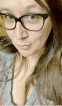 a woman wearing glasses and a blue shirt is taking a selfie .