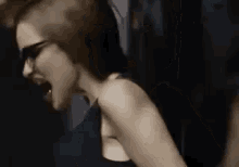 a woman wearing sunglasses is screaming while being tickled by a man in a dark room .