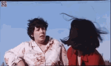 two women are standing next to each other with their hair blowing in the wind . one of the women is wearing a red jacket .