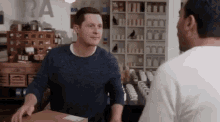 a man in a blue sweater is holding a box in front of another man in a store .