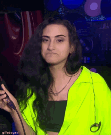 a woman wearing a neon green jacket is holding a microphone