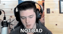 a young man wearing headphones is sitting in front of a microphone and says `` not bad '' .