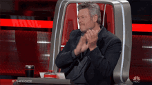a man applauds while sitting in a chair that says nbc